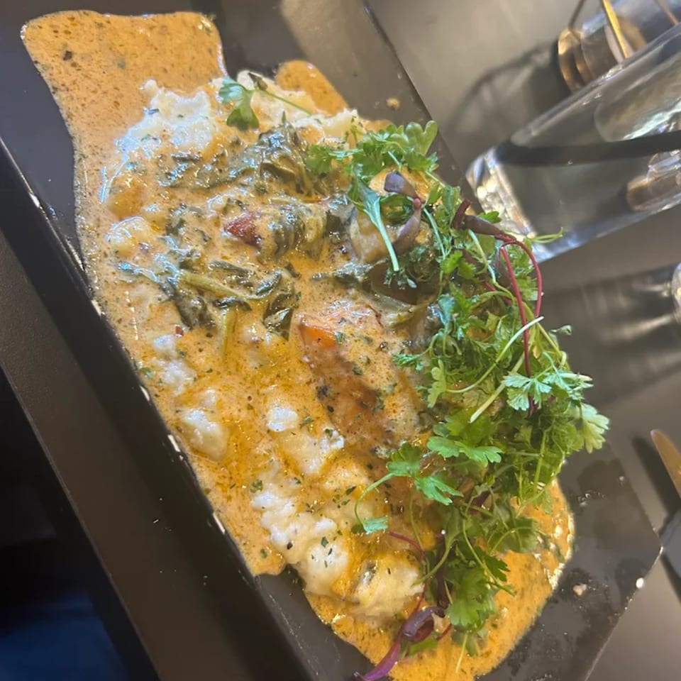 Soul food dish with creamy sauce, greens, and shrimp, garnished with fresh herbs on a black plate.