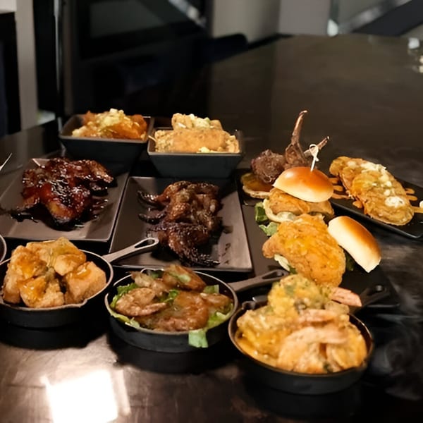 A dark table laden with various soul food dishes, including chicken, shrimp, and sliders.