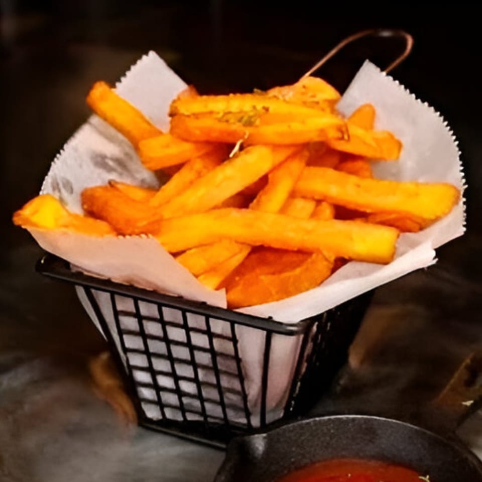 A black wire basket filled with golden-brown sweet potato fries, lined with white parchment paper.
