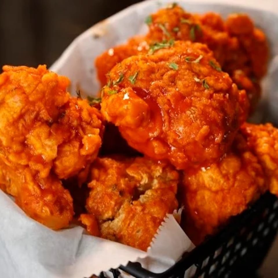 Soule To Soule's crispy, orange-glazed chicken wings, garnished with herbs, served in a black basket.