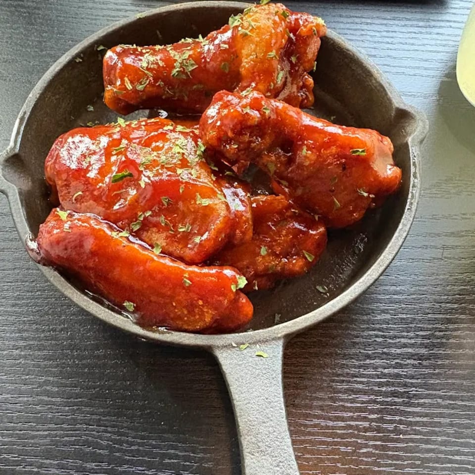 Soule To Soule's sticky, red-glazed chicken wings, sprinkled with herbs, served in a cast-iron skillet.